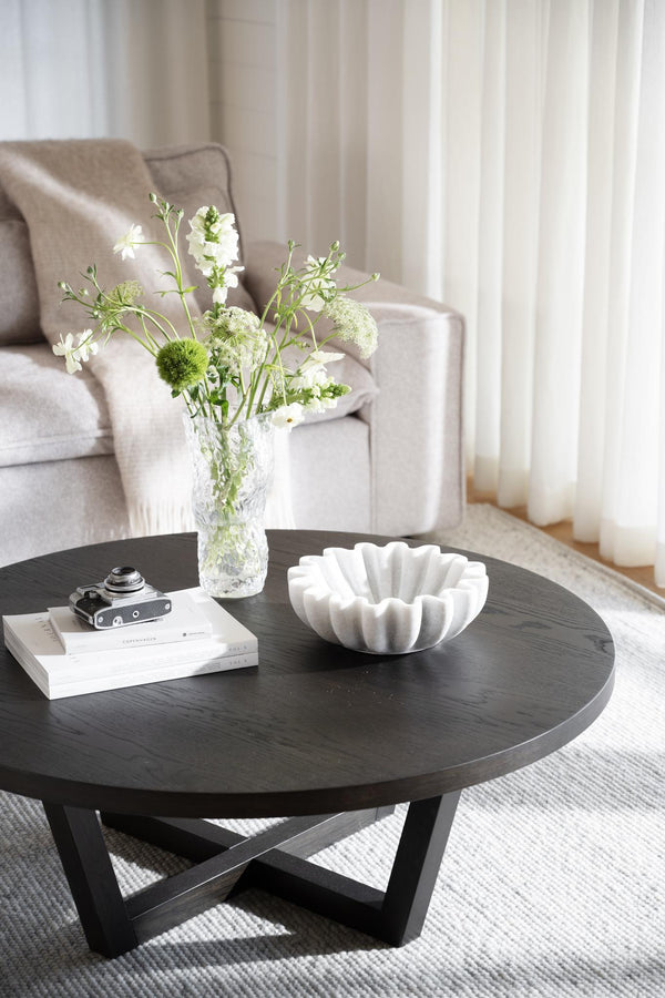 Runt soffbord i mörkt trä med korsade ben, dekorerat med vas med blommor och vit skål