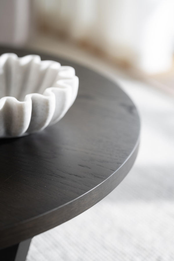 Grå rund träbricka med vit dekorativ skål i vågform, minimalistisk inredningsdetalj för vardagsrum