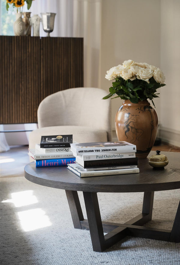 Runt soffbord i mörkt trä med böcker och vas med vita rosor i modernt vardagsrum