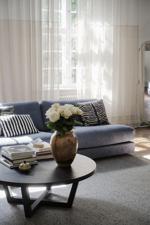 Ljust vardagsrum med blå soffa, svartvitt randiga kuddar, runt soffbord och vita rosor i vas