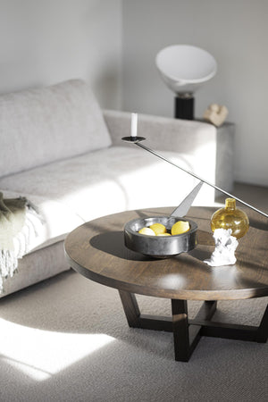 Runt soffbord i mörkt trä med svart metallunderrede, dekorerat med skål, ljusstake och gul vas