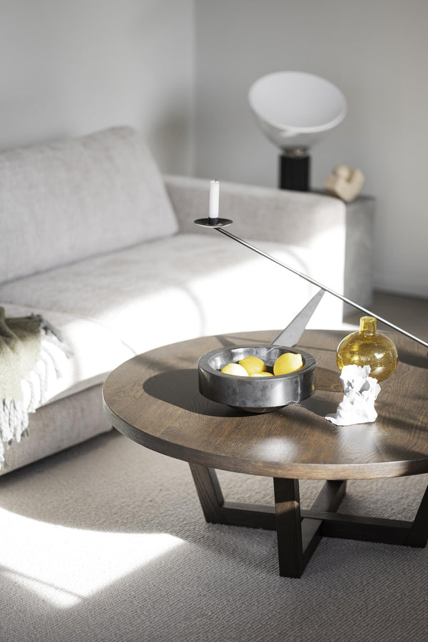 Runt soffbord i mörkt trä med svart metallunderrede, dekorerat med skål, ljusstake och gul vas