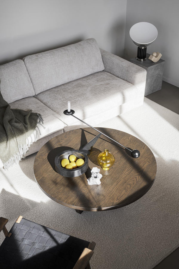 Runt soffbord i mörk ek med dekorativa föremål, grå soffa och modern lampa i minimalistisk vardagsrumsinredning