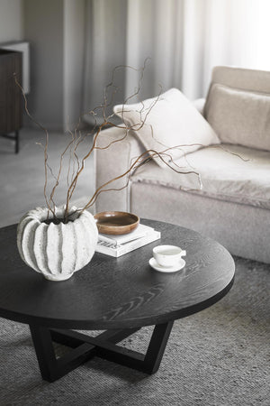 Runt soffbord i svart trä med vit räfflad vas, dekorativa kvistar och kaffekopp i minimalistisk stil