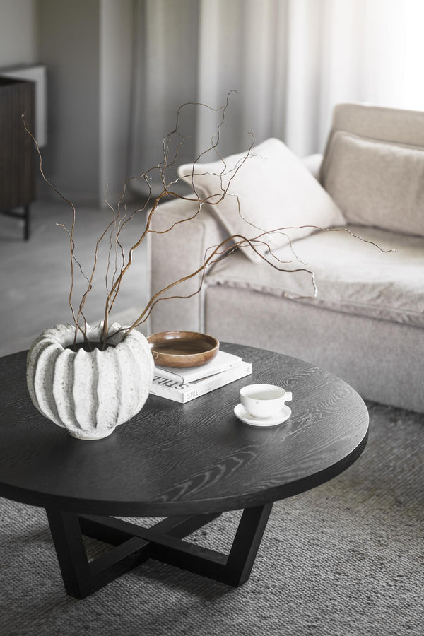 Runt soffbord i svart trä med vit räfflad vas, dekorativa kvistar och kaffekopp i minimalistisk stil