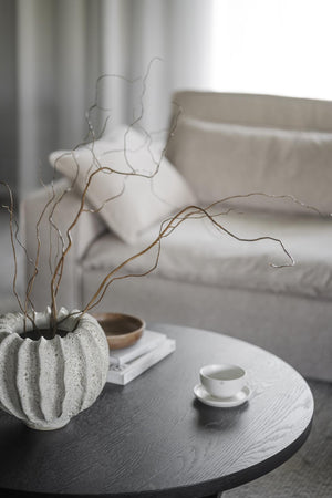 Grå spräcklig keramikvas med dekorativa kvistar på runt soffbord i vardagsrum med vit kaffekopp