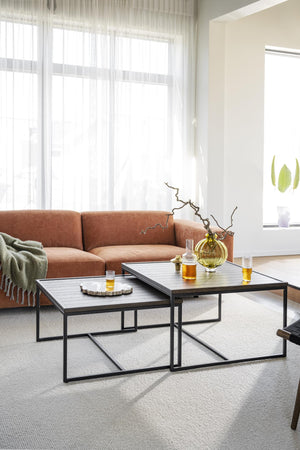 Soffbord i set med svart metallram och träskiva, stylat med gula glasdekorationer framför terrakottafärgad soffa