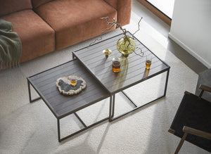 Soffbord i mörkt trä med metallben, två nivåer med glasdetaljer och dekorativa föremål i modernt vardagsrum