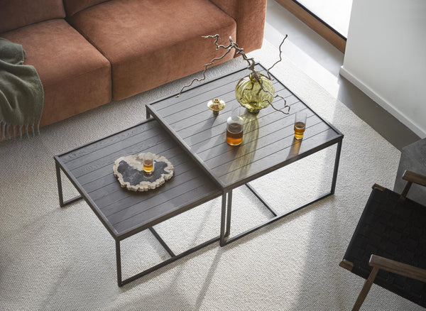 Soffbord i mörkt trä med metallben, två nivåer med glasdetaljer och dekorativa föremål i modernt vardagsrum