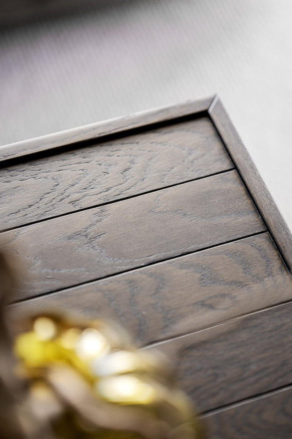 Närbild på mörkgrå träkommod med synlig trästruktur och dekorativ gulddetalj i förgrunden