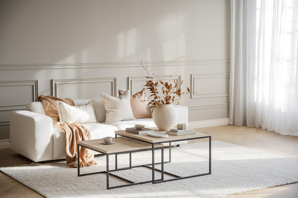 Ljust vardagsrum med vit soffa, beige kuddar, två soffbord i trä och metall, och höstdekoration