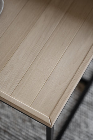 Närbild på ljus träskiva med synlig trästruktur och slät yta, monterad på metallben