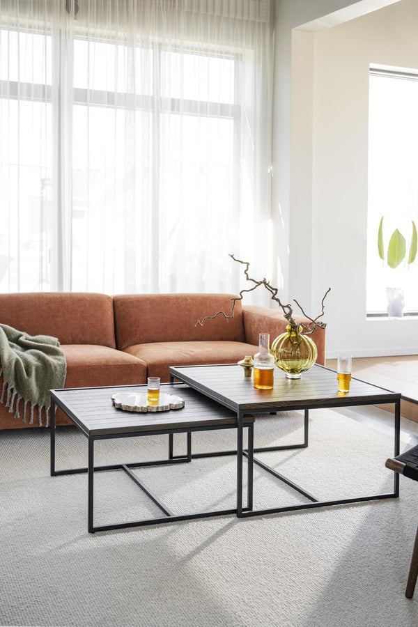 Soffbord i set med svart metallram och träskiva framför terrakottafärgad soffa i ljust vardagsrum