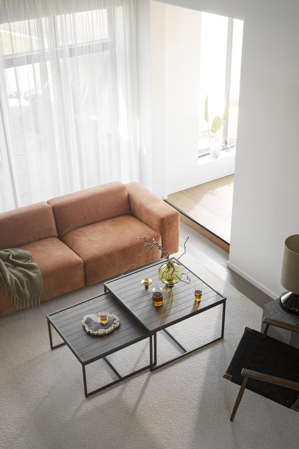 Modernt vardagsrum med terrakottafärgad soffa, svarta soffbord i metall och ljusa gardiner vid fönster