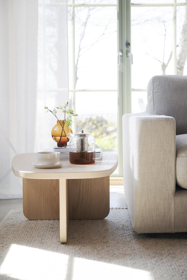 Ljust vardagsrum med runt soffbord i trä och marmor, grå soffa och tepanna vid fönster