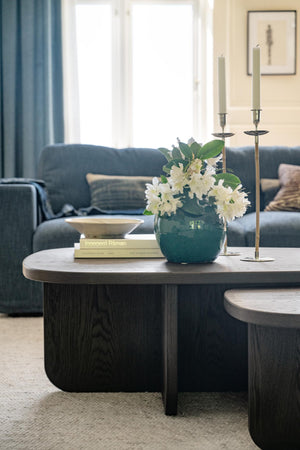 Oval soffbord i mörkt trä med vaser, ljusstakar och bok i modernt vardagsrum med blå soffa