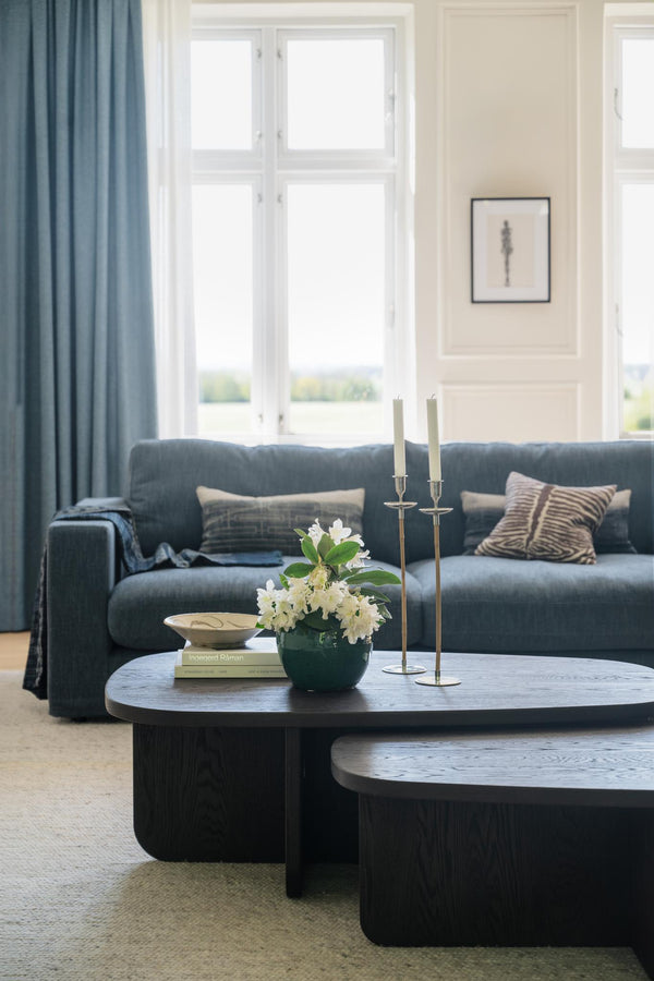 Elegant vardagsrum med blå sammetssoffa, svarta runda soffbord och mässingsljusstakar