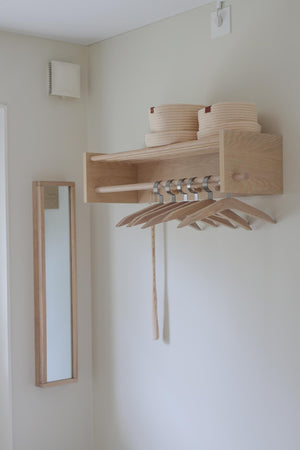 Minimalistisk väggmonterad hallhylla i ljust trä med spegel, krokar och förvaringskorg