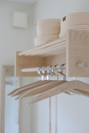 Ljust trähyllsystem med galge för kläder och flätade förvaringskorg i naturliga toner