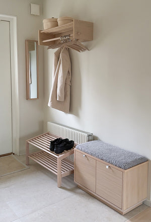 Ljus hallmöbel i trä med bänk, skohylla och klädhängare monterad på väggen i modern skandinavisk stil