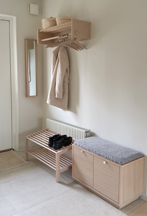 Ljus hallmöbel i trä med bänk, skohylla och klädhängare monterad på väggen i modern skandinavisk stil