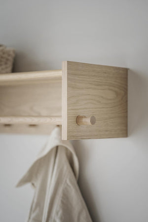 Klädhängare i ljust trä med enkel design monterad på vit vägg, med beige textil hängande på kroken