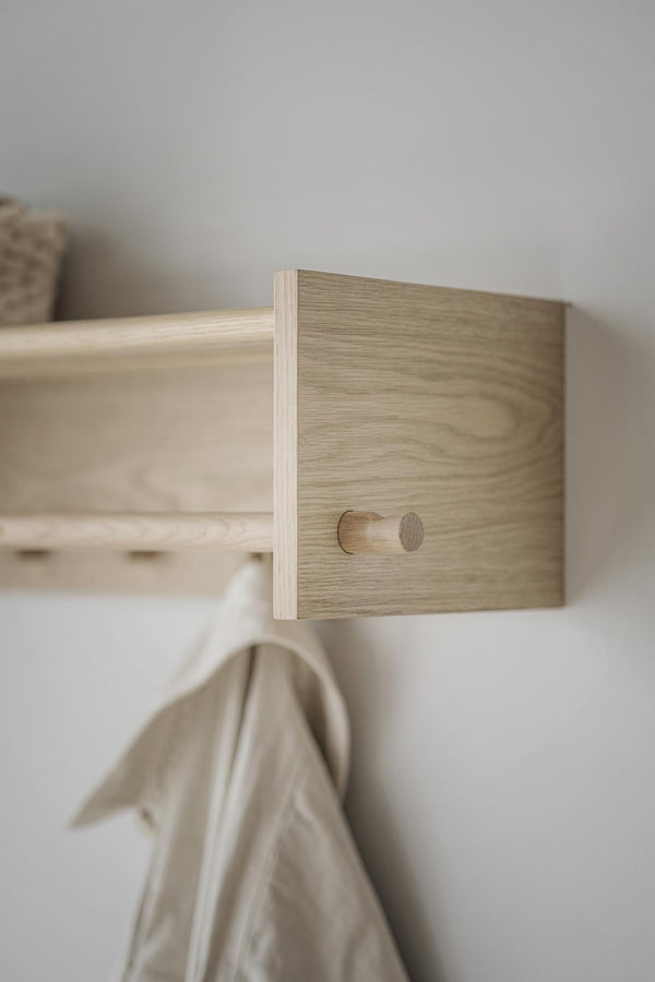 Klädhängare i ljust trä med enkel design monterad på vit vägg, med beige textil hängande på kroken