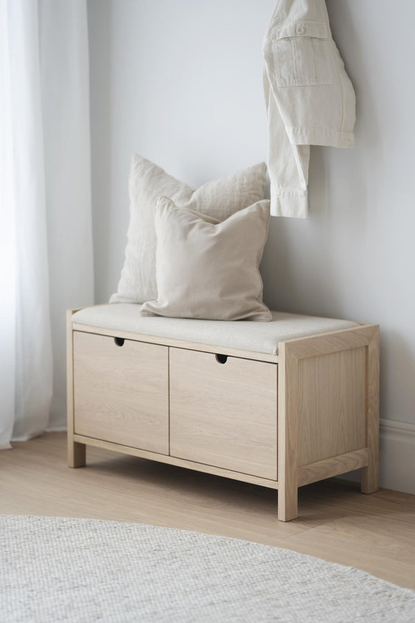 Ljus träbänk med förvaringslådor och vita kuddar i minimalistisk entré