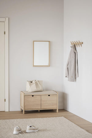 Minimalistisk hall med hallmöbel i ljust trä, spegel, krokbräda och vit väggfärg i skandinavisk stil