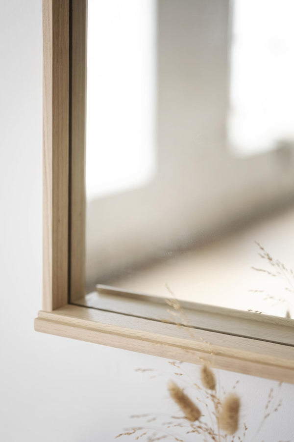 Spegel med ljus träram i naturligt trä och inbyggd hylla, närbild av hörn