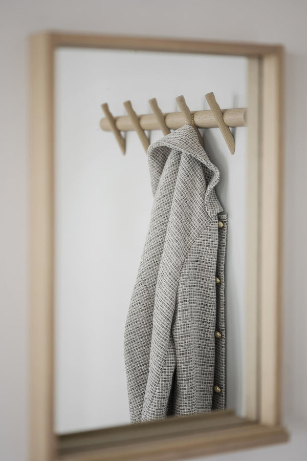 Klädhängare i ljust trä monterad på vit vägg med grå rutigt plagg upphängt