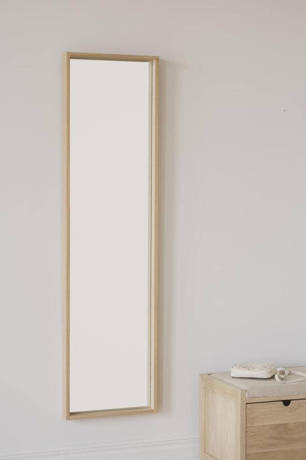 Smal spegel med ljus träram i furu monterad på vit vägg bredvid litet träbord med dekorationer