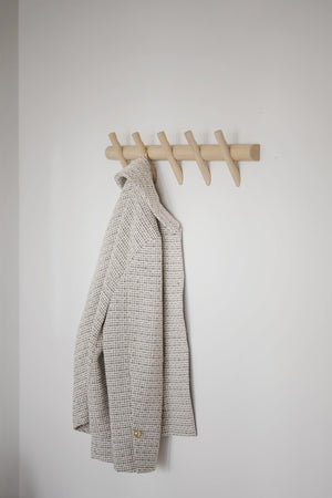 Beige klädhängare i trä med fem krokar på vit vägg, med en grå rutig kavaj upphängd