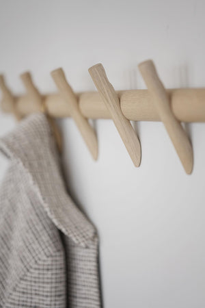 Klädhängare i ljust trä med beige rutigt tyg upphängt på vägghängare i minimalistisk stil