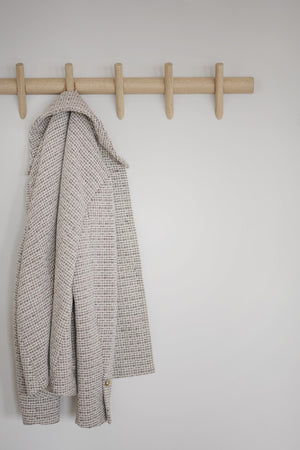 Beige rutigt kavajer hängande på träkroklist med fem krokar mot vit vägg