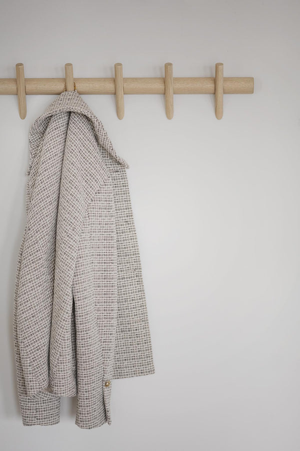 Beige rutigt kavajer hängande på träkroklist med fem krokar mot vit vägg