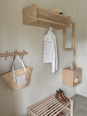 Ljust trä hallmöbel med hyllor, krokar och spegel i modern skandinavisk stil med vit jeansjacka och väska