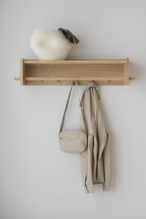 Väggmonterad hattshylla i ek med krokar, dekorerad med korg och väska i beige toner