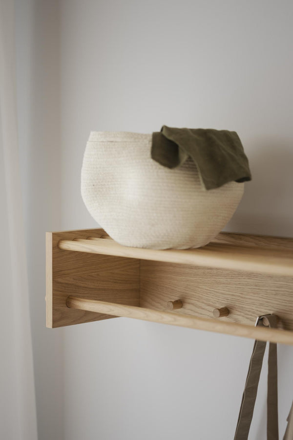 Vit keramikskål med olivgrön handduk på ljus träväggshylla med krokar