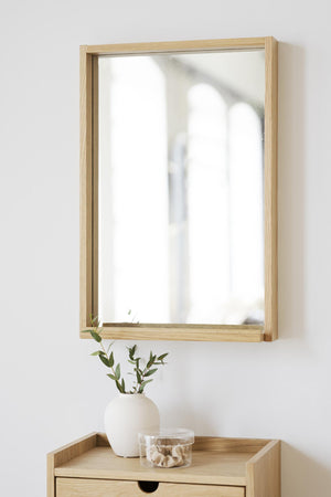 Spegel med ljus ekram ovanför byrå med vas och dekoration i minimalistisk skandinavisk stil