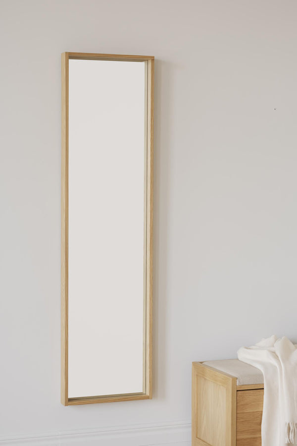 Smal spegel med ljus träram i ek hängande på vägg bredvid träbänk med filt