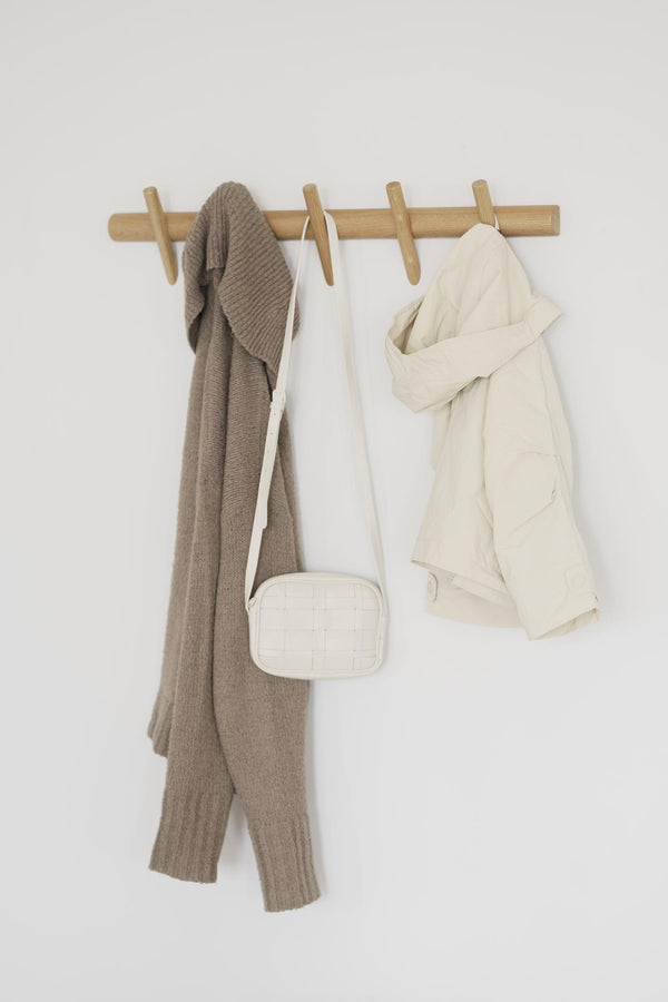 Klädhängare i trä med fyra krokar med beige kofta, vit väska och vit jacka upphängda