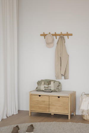 Halkappa och jacka hängande på träkrokar ovanför bänk med duffelväska i minimalistisk hall