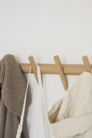Krokställning i ljust trä med fyra krokar, med hängande kläder i beige och vitt mot vit vägg