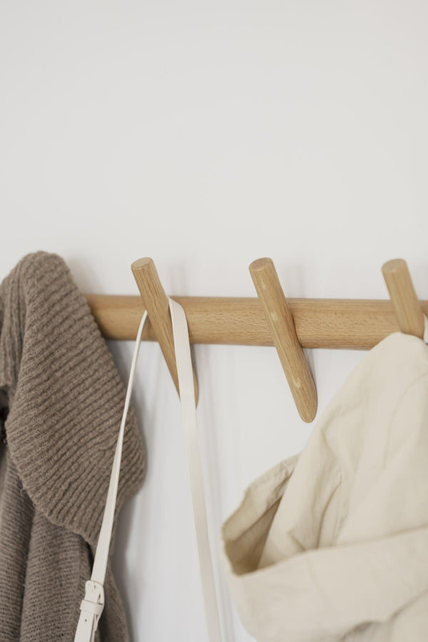 Krokställning i ljust trä med fyra krokar, med hängande kläder i beige och vitt mot vit vägg