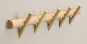Krokplanka i ljust trä med fem snedställda krokar monterad på vit vägg