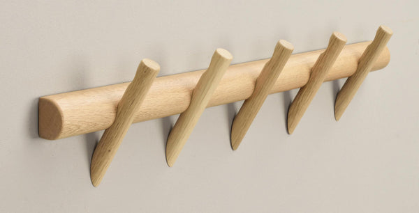 Krokplanka i ljust trä med fem snedställda krokar monterad på vit vägg