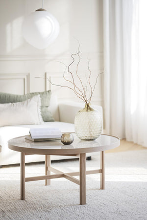 Runt soffbord i ljust trä med glasvas, bok och dekoration i skandinavisk stil