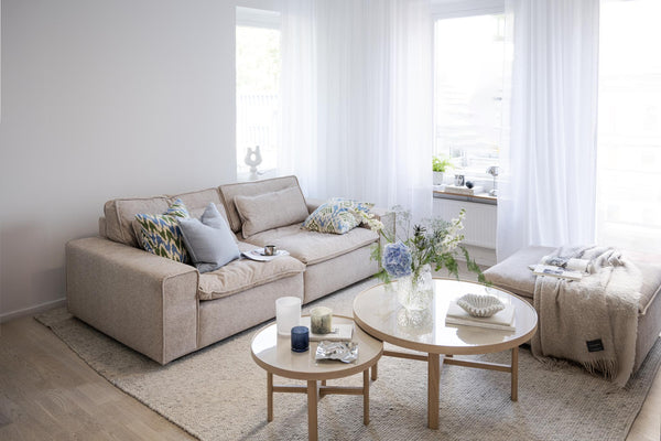 Ljust vardagsrum med beige soffa, runda soffbord i trä och vita gardiner