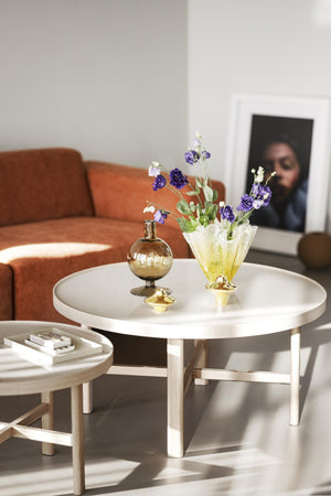 Runt vitt soffbord med glasvas med lila blommor och dekorativ parfymflaska i vardagsrum med orangebrun soffa